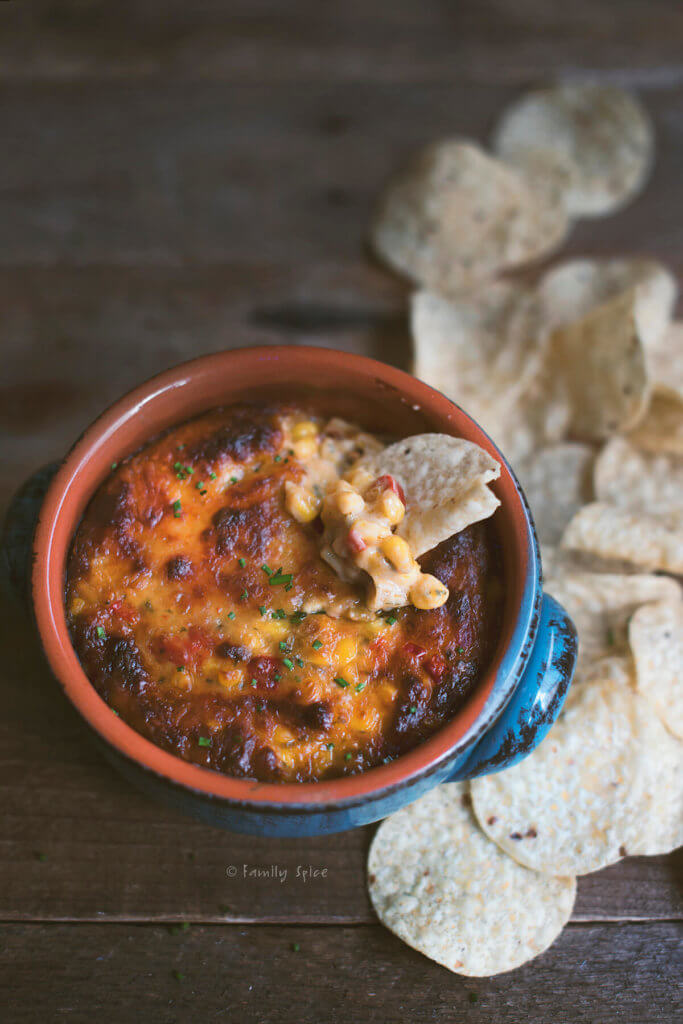 Cheesy hatch chile corn dip in a rustic blue bowl with chips in it and around it