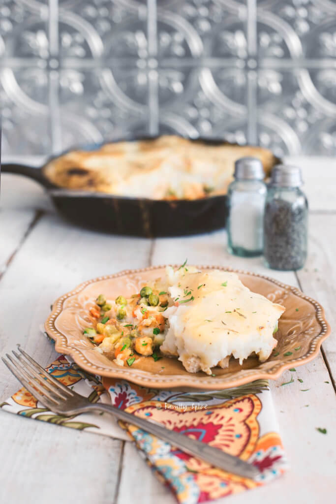 A serving of chicken shepherds pie on a yellow plate with a cast iron pan with the remaining behind it