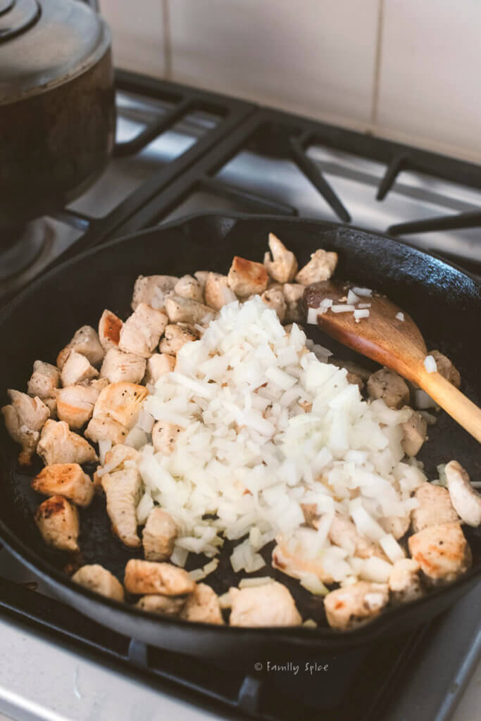 Adding chopped onions to browned chicken breast in a cast iron pan