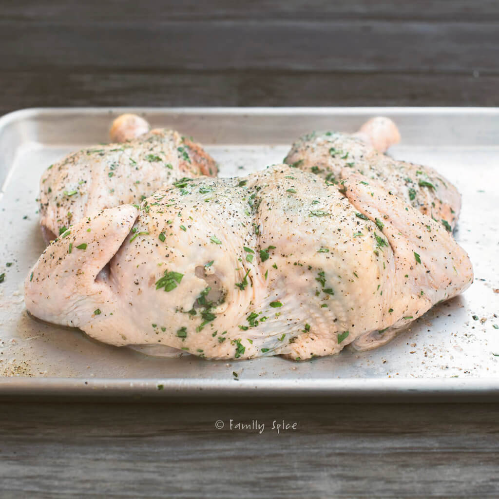 Side view of a raw spatchcocked chicken smothered in herbs on a baking sheet