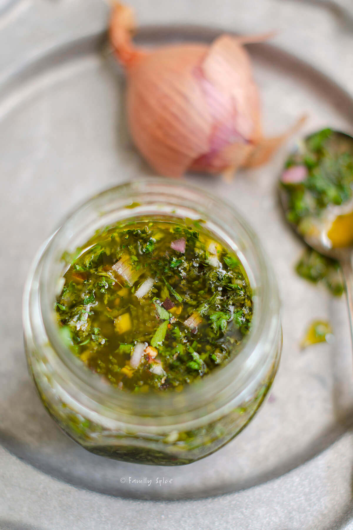 Some herb olive oil marinade in a mason jar with a shallot behind it