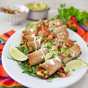 Closeup of baked steak taquitos on a white plate garnished with guacamole, pico de gallo and sour cream.