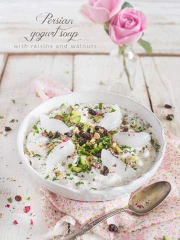 A bowl of Persian cold yogurt soup topped with rose petals, herbs and ice cubes by FamilySpice.com