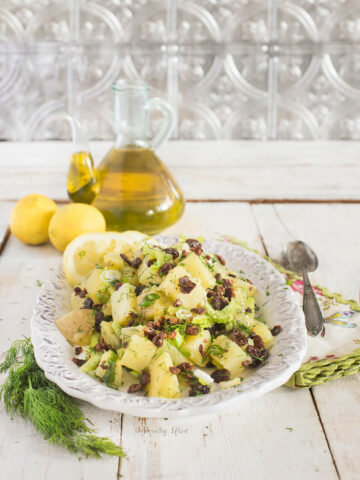Side view of an olive oil potato salad with lemons and bottle of olive oil behind it