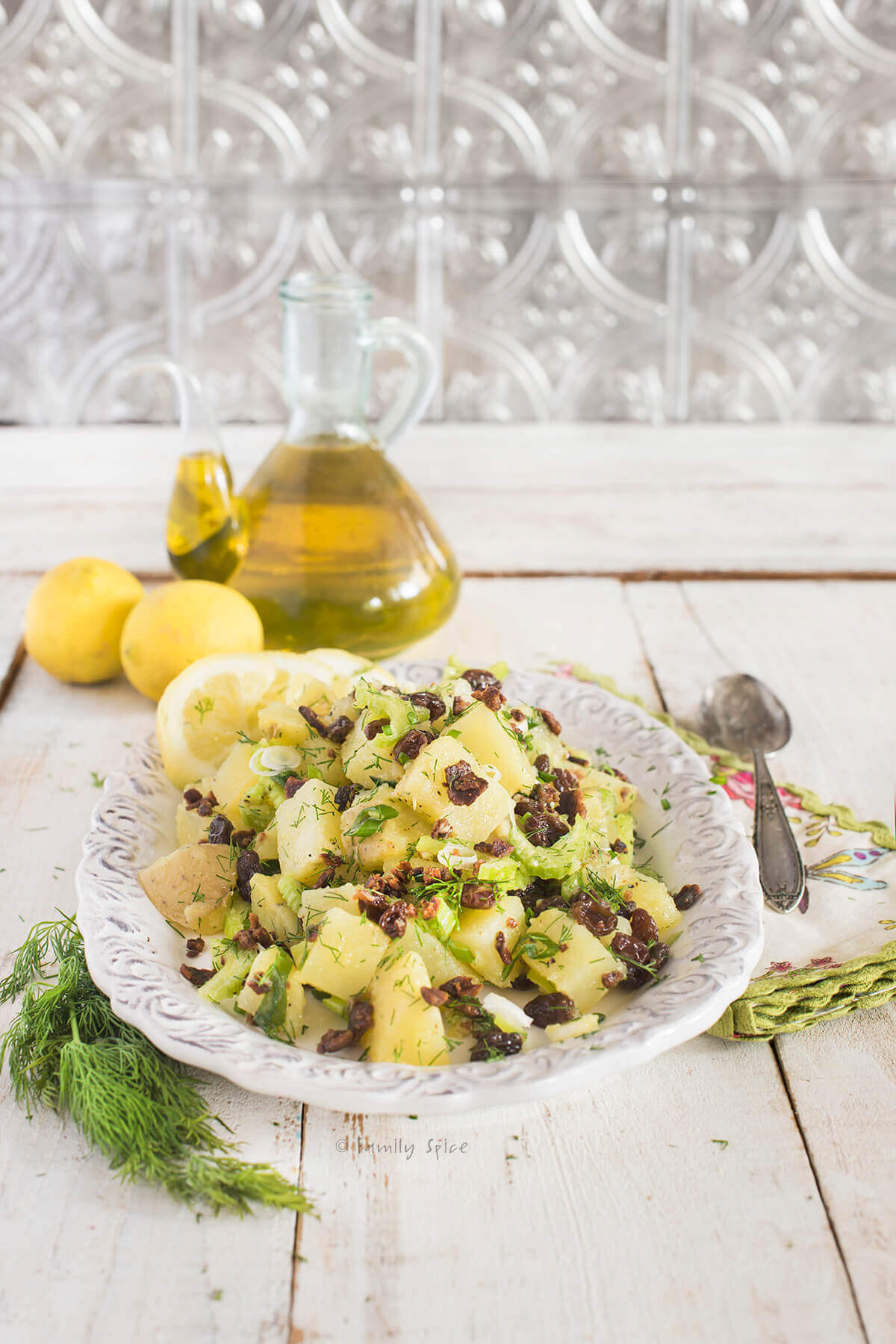 Side view of an olive oil potato salad with lemons and bottle of olive oil behind it