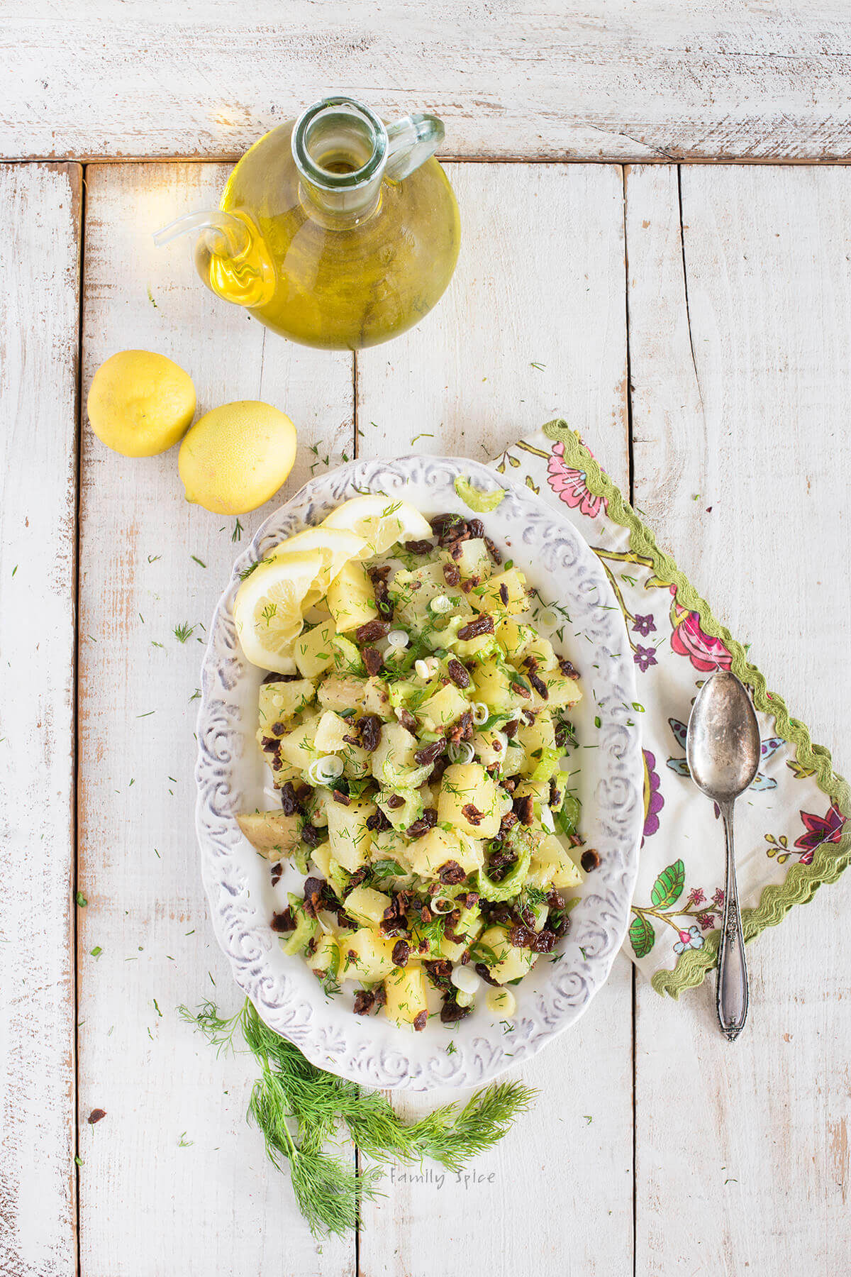 Top view of an olive oil potato salad with lemons and bottle of olive oil next to it