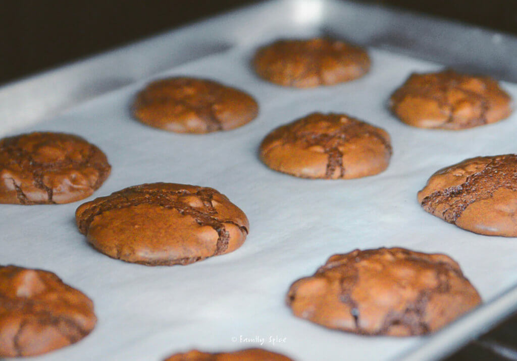 Brownie cookies baking on a baking sheet lined with parchment paper in the oven