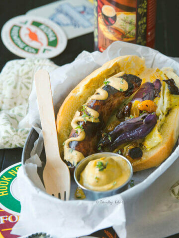 Oven baked bratwurst on a hoagie with mustard, roasted cabbage and red onions in a hoagie roll and in a metal food basket