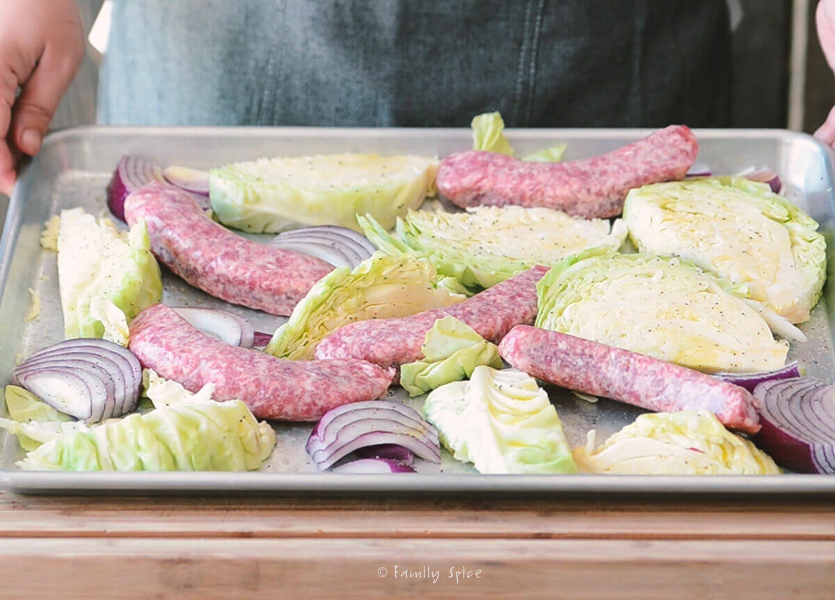 Brats with wedges of cabbage and red onions on a baking sheet ready to bake in the oven