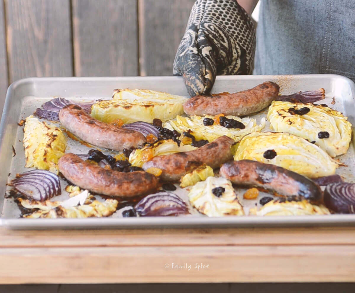 A baking sheet with freshly baked brats with onions and cabbage and raisins