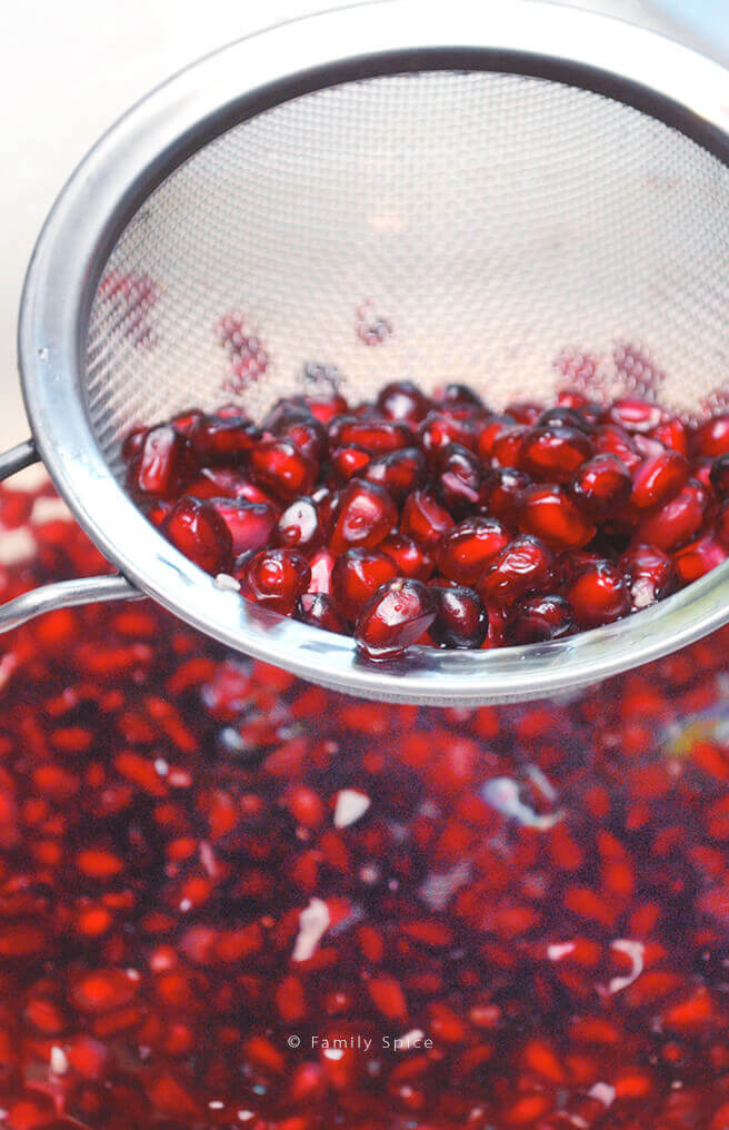 Pomegranate arils getting strained out of bowl of water by FamilySpice.com