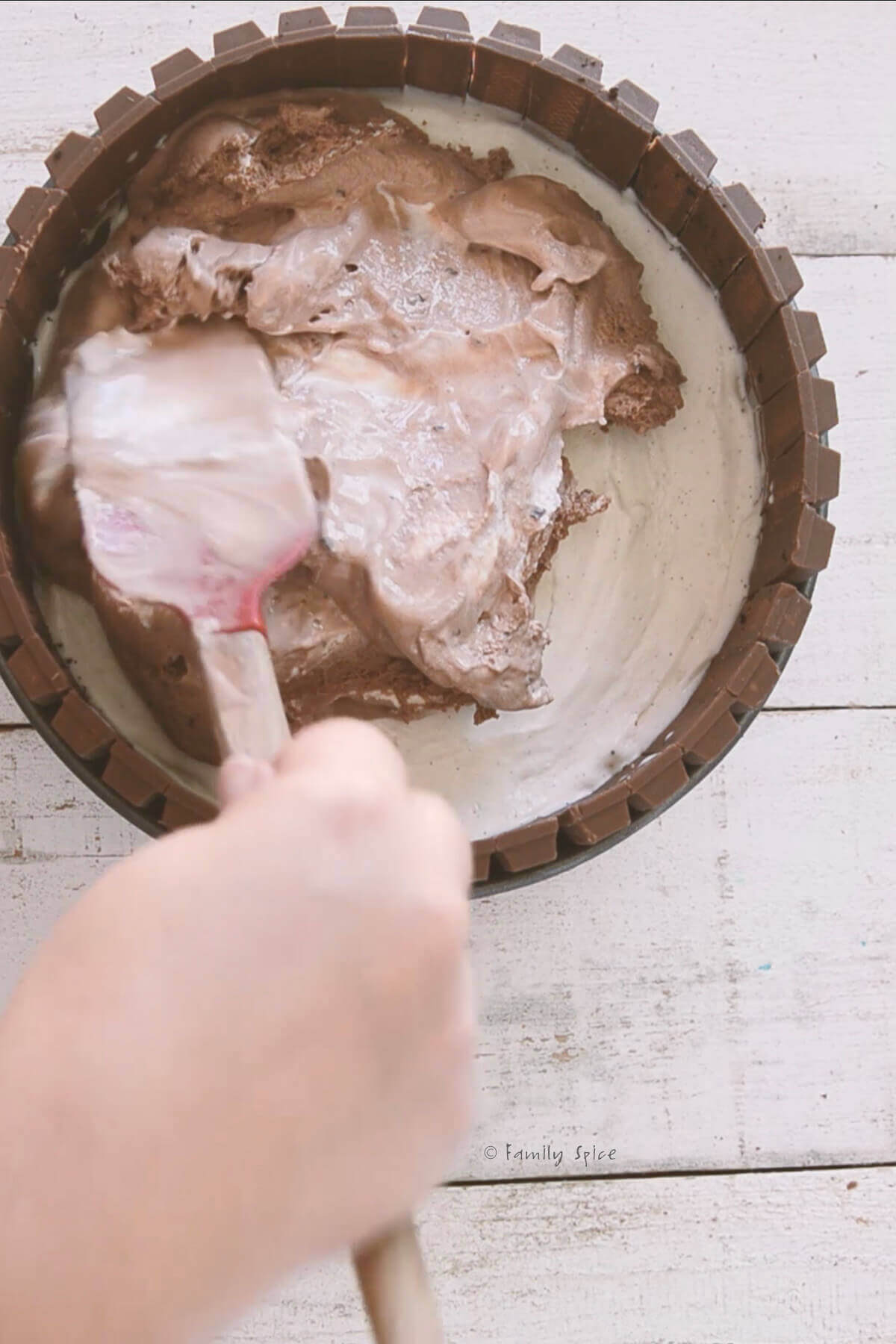 Spreading chocolate ice cream over vanilla ice cream inside a springform pan to make an ice cream cake