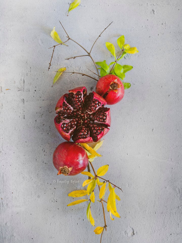A cut open pomegranate with two other pomegranates and a tree branch.