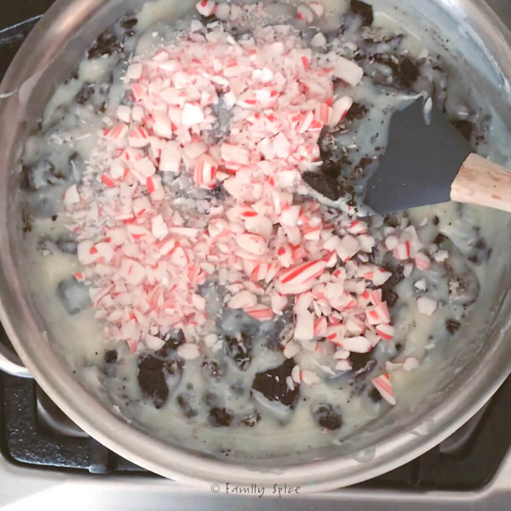 Crushed peppermints stirred into melted white chocolate mixture in a stainless pot