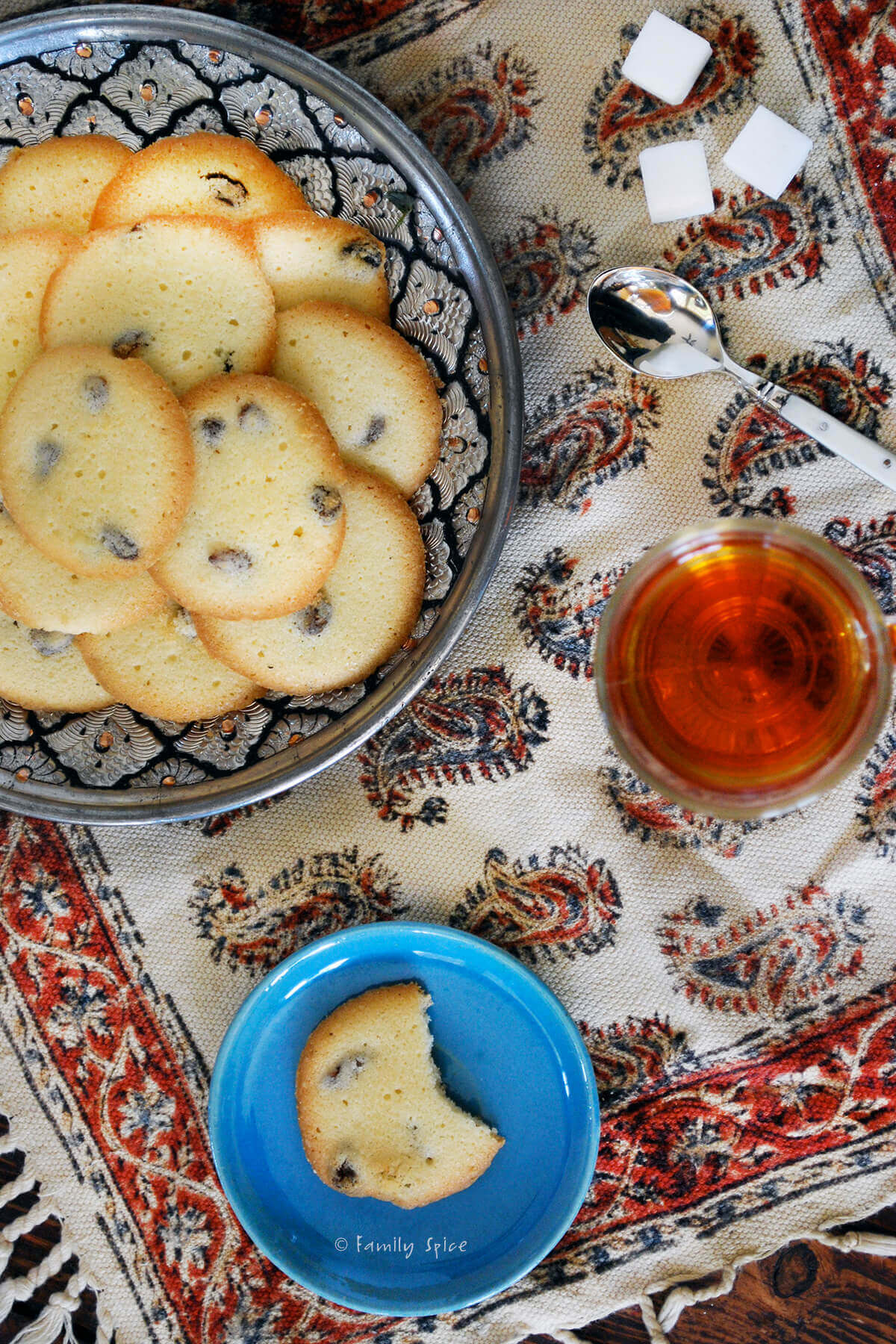 A Persian table cloth with a plate of saffron cookies on it and a glass of hot tea