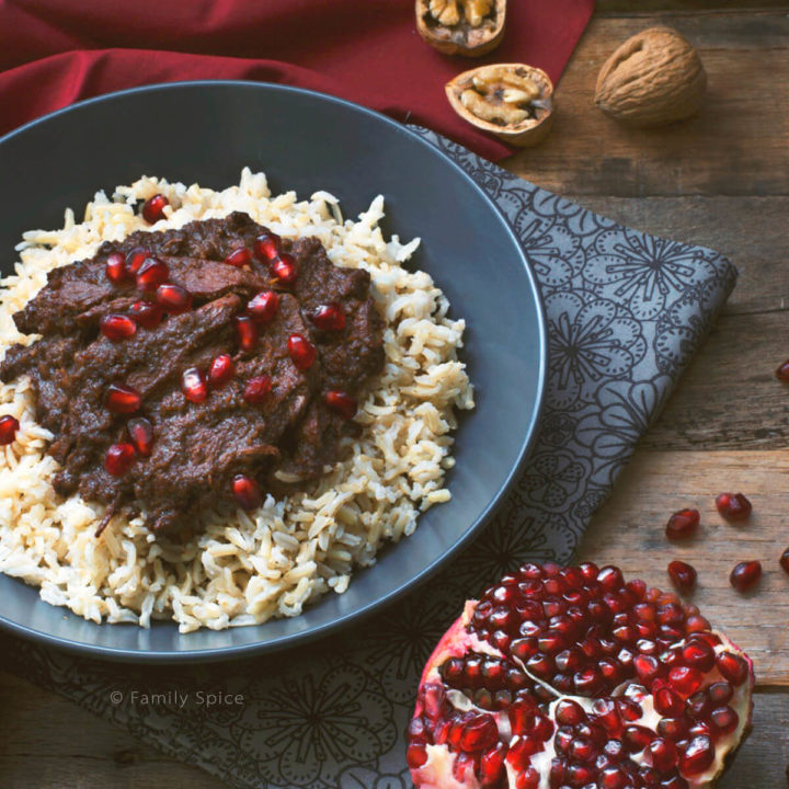 A bowl of Persian Pomegranate and Walnut Stew (Fesenjan) over brown rice next to half a pomegranate
