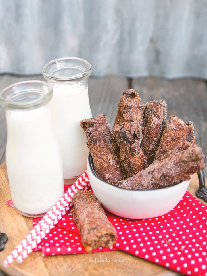 A bowl of fried cinnamon raisin bread rollups with a couple of bottles of milk on a red napkin on a tray