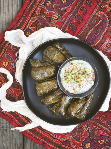 Overhead shot of a plate full of Persian dolma (or dolmeh/dolmades), stuffed grape leaves with a bowl of yogurt dip