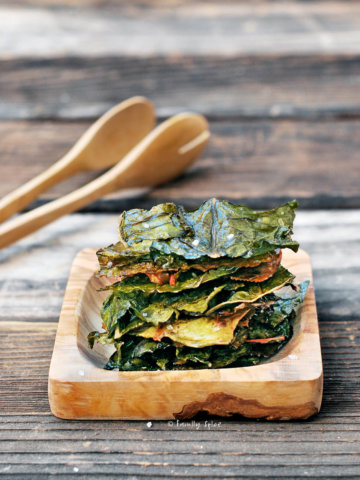 Baked chard chips stacked on a wooden square plate