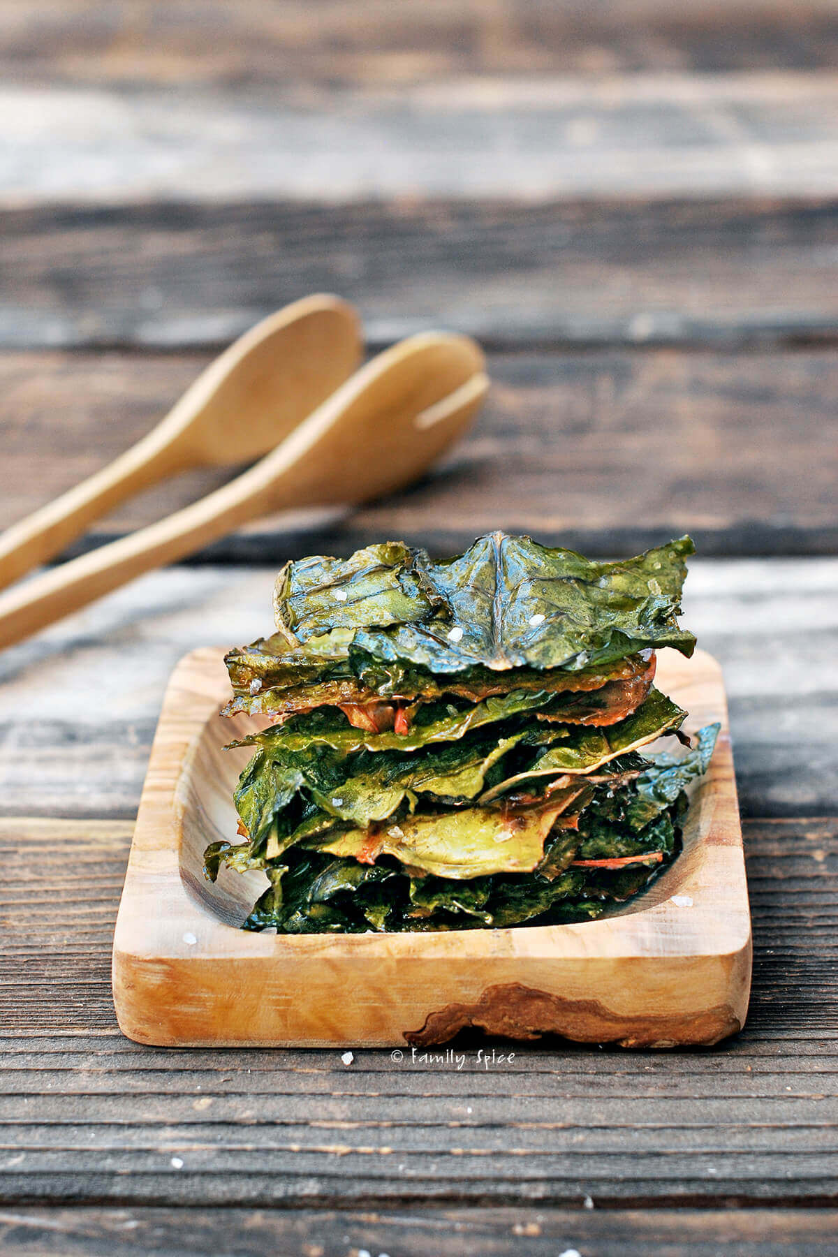 Baked chard chips stacked on a wooden square plate