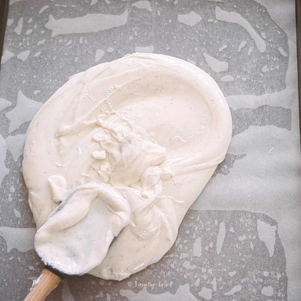 Melted white chocolate being spread onto a sheet pan lined with parchment paper