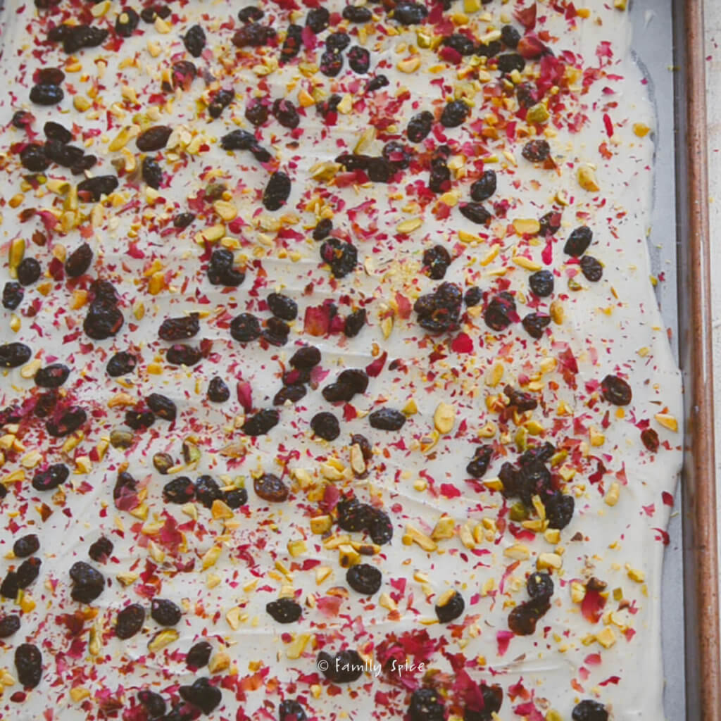 Raisins, rose petals and pistachios topped onto melted chocolate in a sheet pan