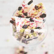 White chocolate bark topped with pisatchios, raisins and rose petals broken up and in a wine glass