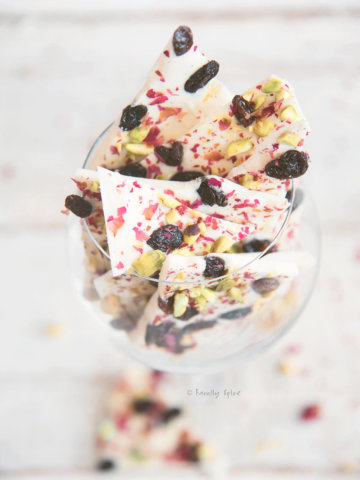 White chocolate bark topped with pisatchios, raisins and rose petals broken up and in a wine glass