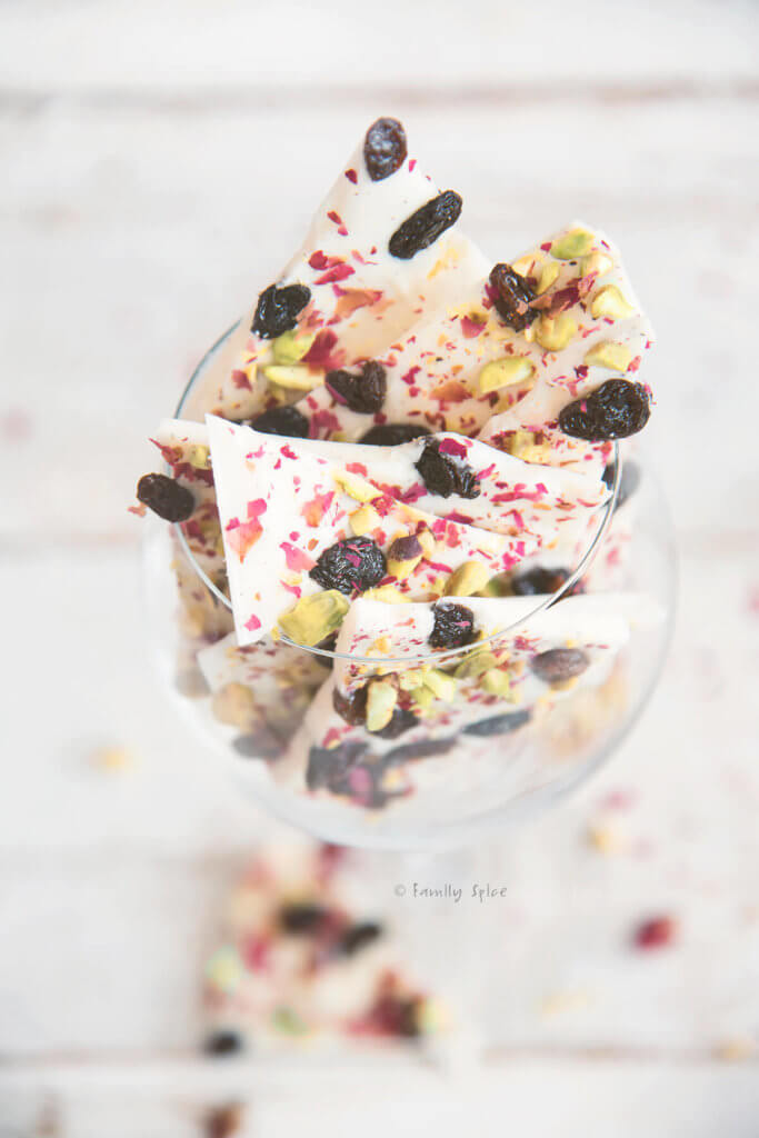 White chocolate bark topped with pisatchios, raisins and rose petals broken up and in a wine glass