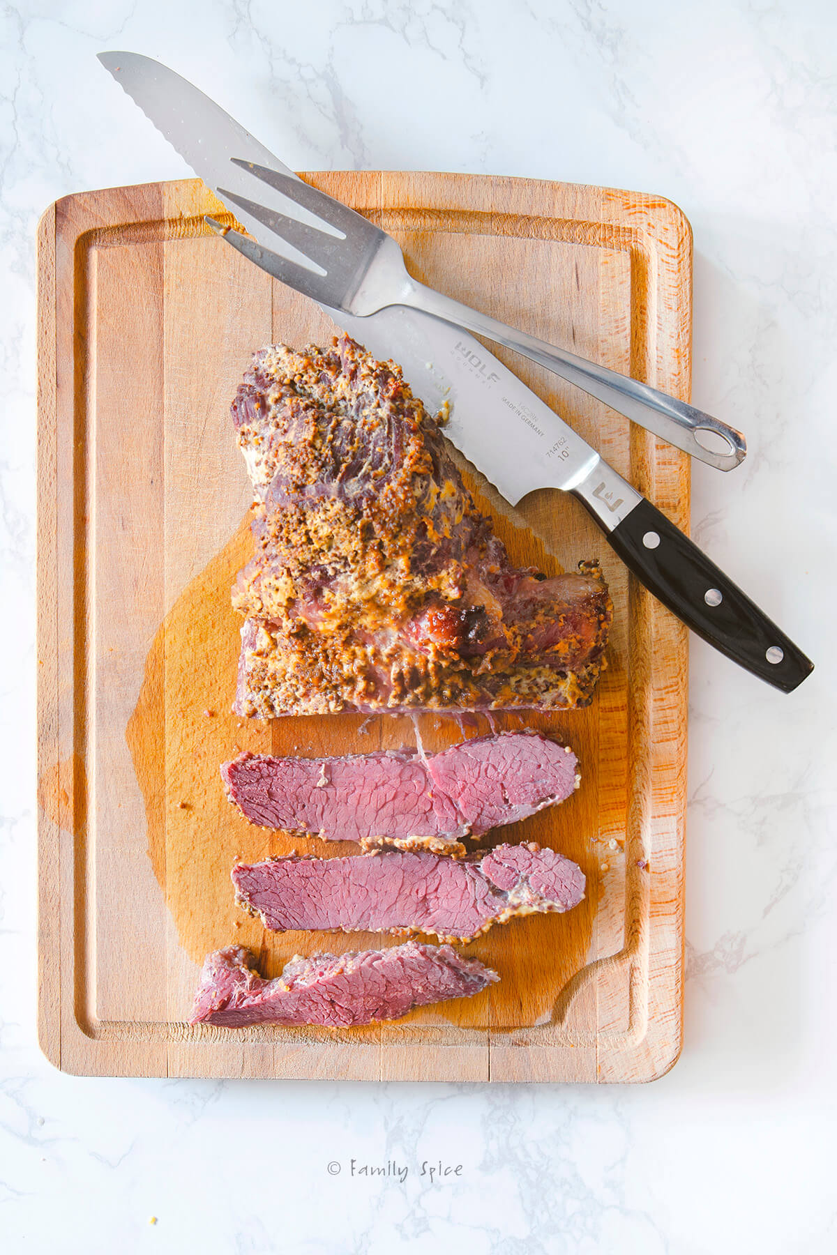 A baked corned beef brisket on a cutting board with a knife and fork and slices of meat