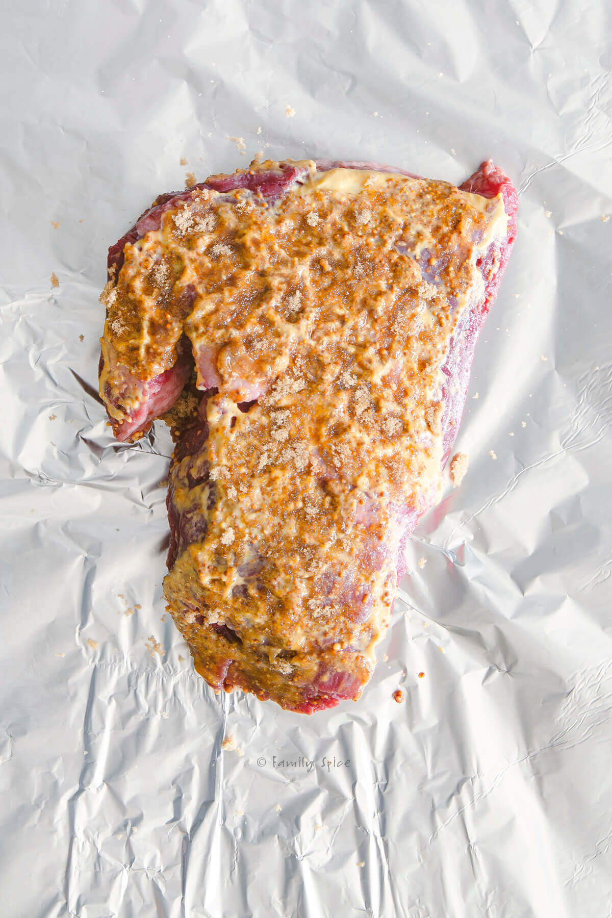 Corned beef brisket covered in mustard and brown sugar on a sheet of foil