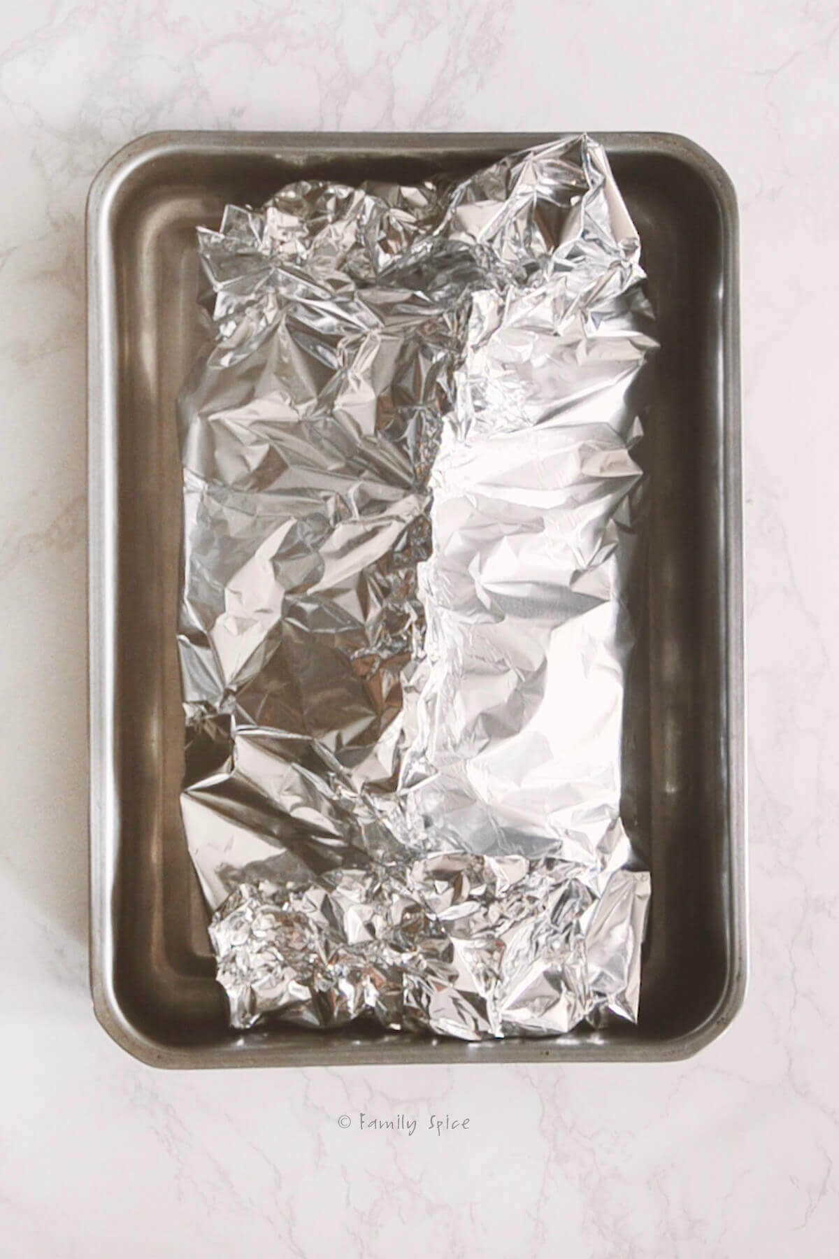 A corned beef roast wrapped in foil in a baking pan