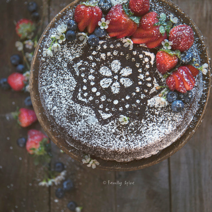 Closeup of a gingerbread cake dusted with powdered sugar and topped with berries