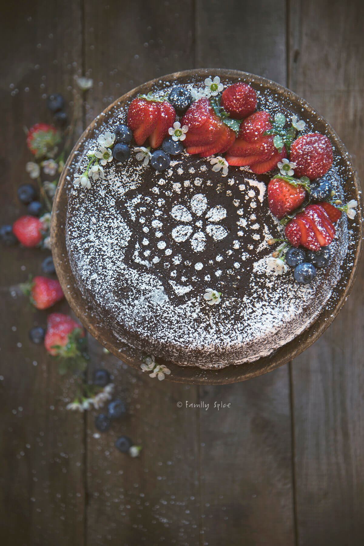 Closeup of a gingerbread cake dusted with powdered sugar and topped with berries