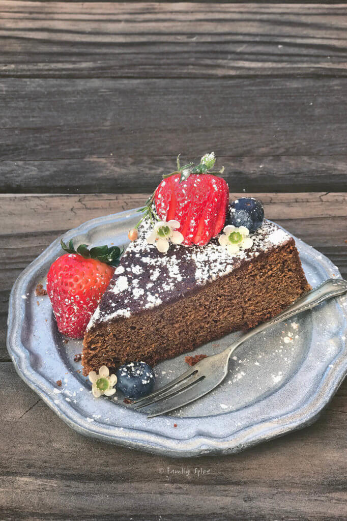 A slice of gingerbread cake on a pewter plate topped with powdered sugar and berries