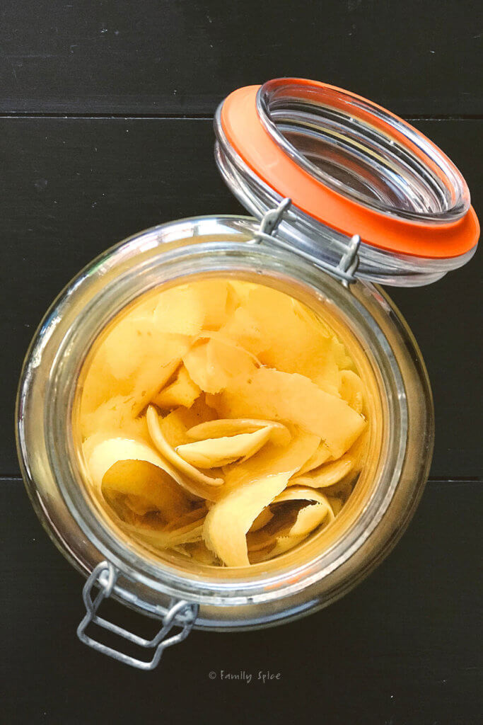 Top view of a large mason jar with lemon peels and vodka to make homemade limoncello