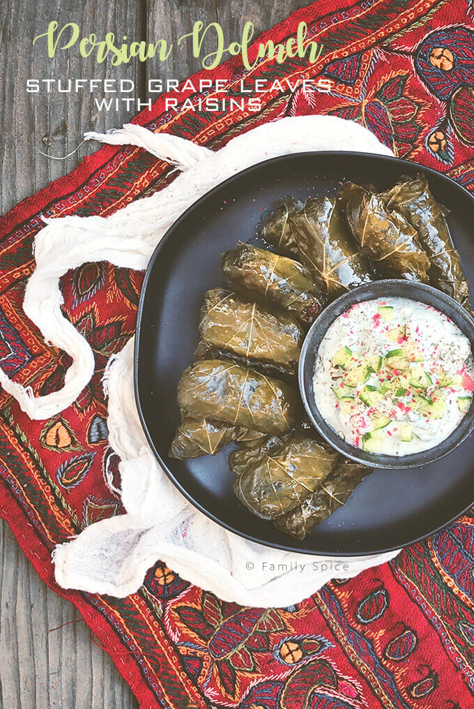 Overhead shot of a plate full of Persian dolma (or dolmeh/dolmades), stuffed grape leaves with a bowl of yogurt dip - FamilySpice.com