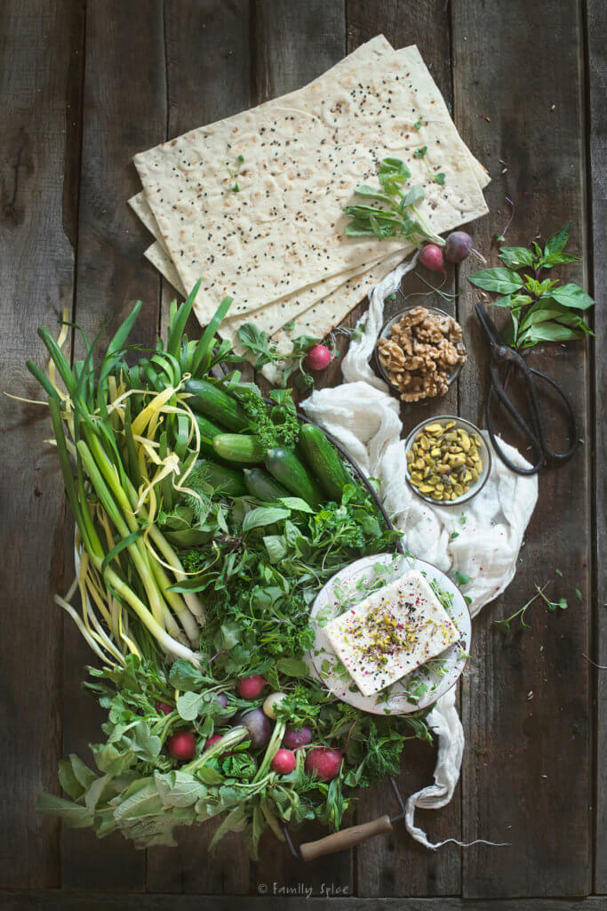 An array of fresh herbs (sabzi khordan) and radishes with a plate of feta, some lavash bread and bowls of nuts