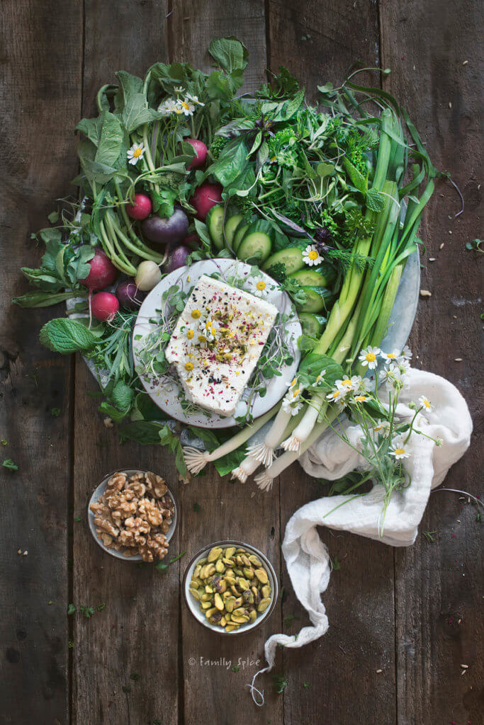 An array of fresh herbs (sabzi khordan)and radishes with a plate of feta and bowls of nuts