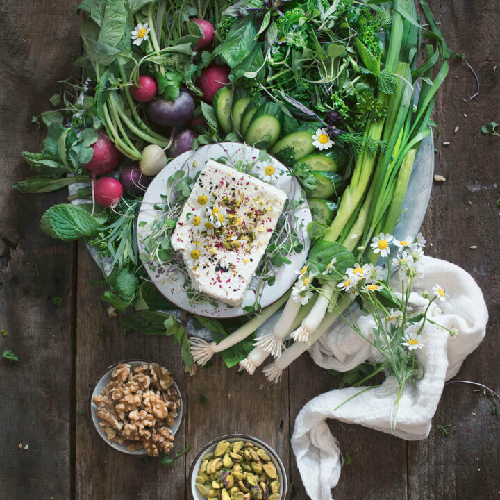 An array of fresh herbs (sabzi khordan)and radishes with a plate of feta and bowls of nuts