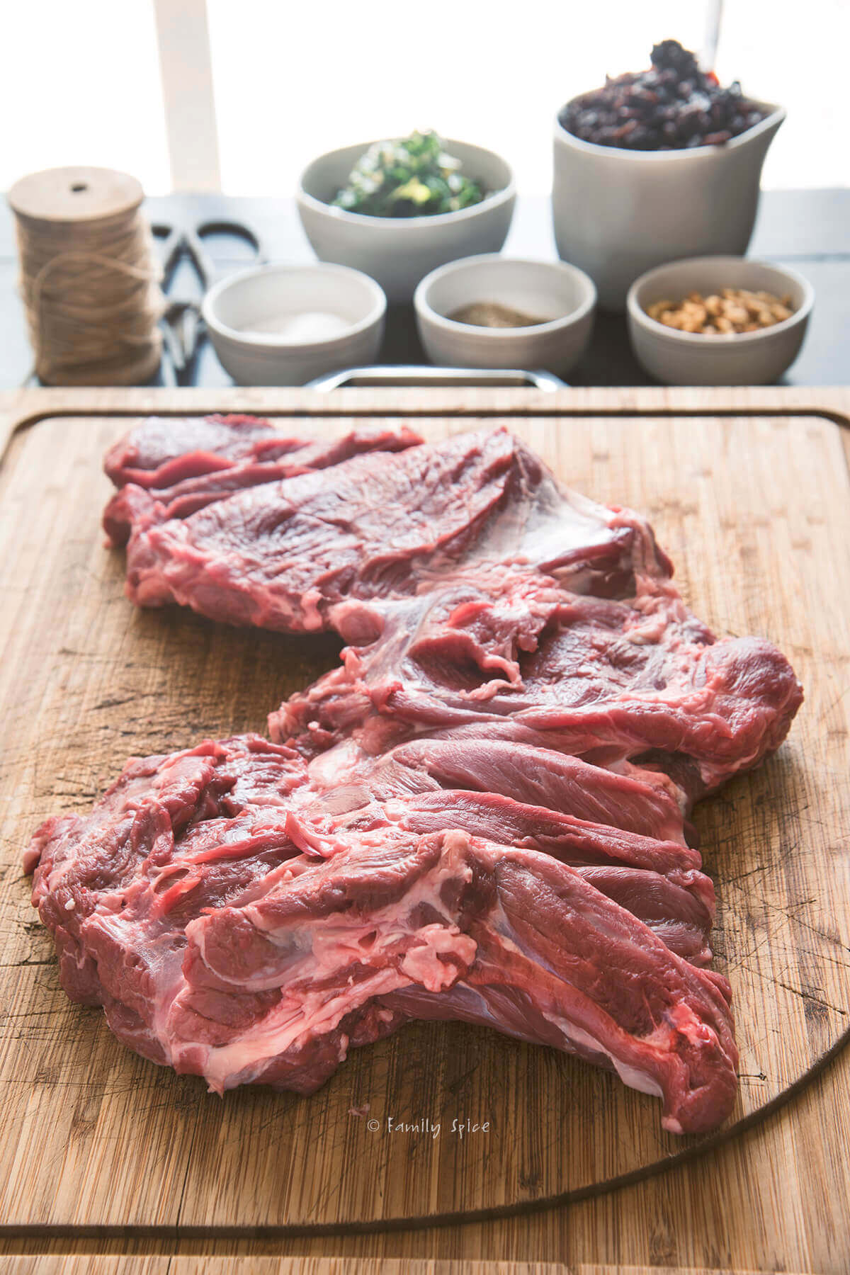 A boneless leg of lamb butterflied and flattened on a cutting board with ingredients around it