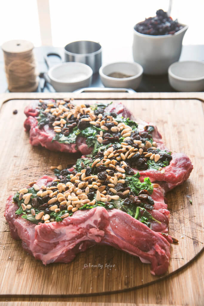A boneless leg of lamb butterflied and flattened on a cutting board with spinach, raisins and pine nuts on top