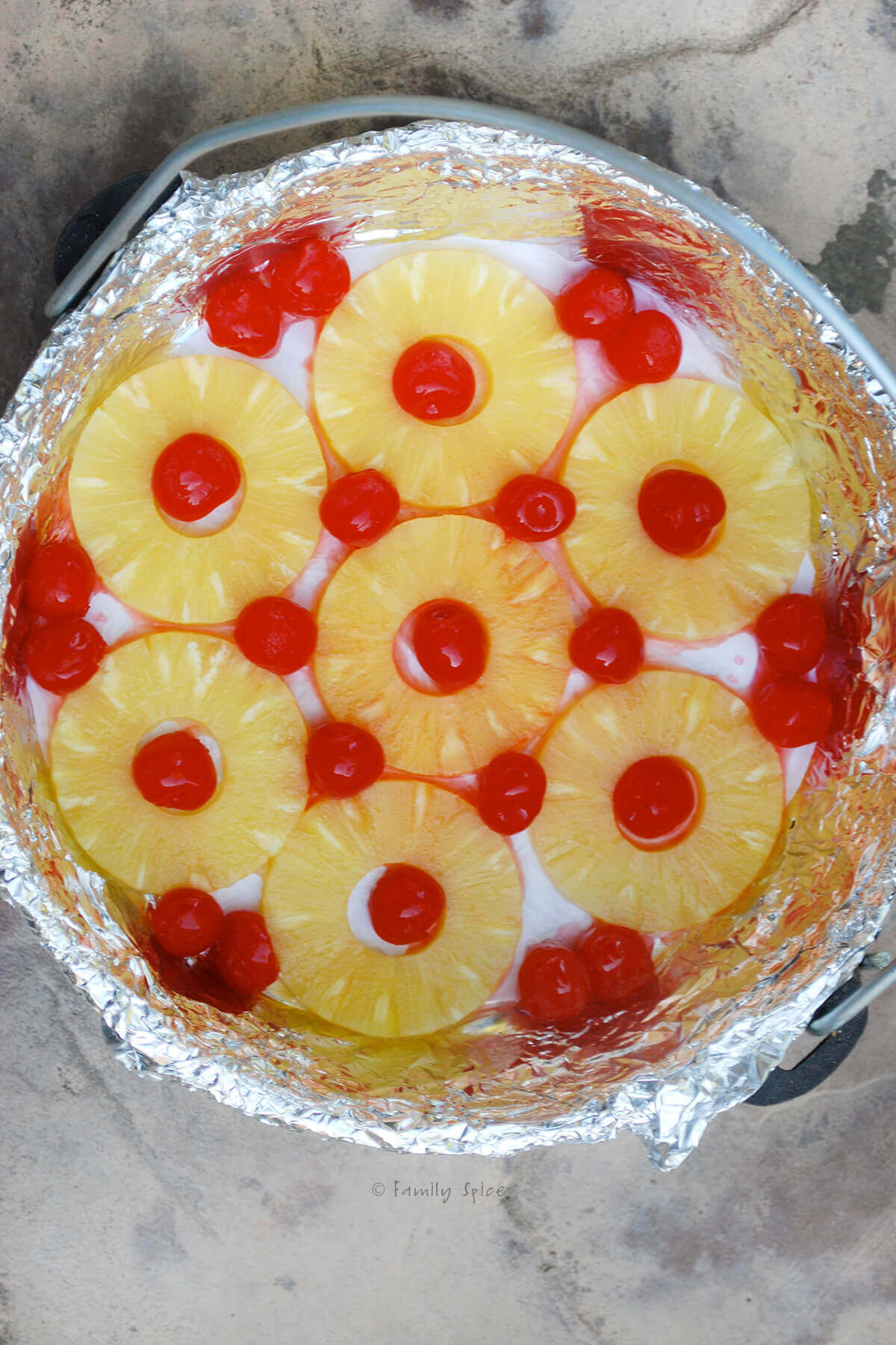 Top view of a Dutch oven lined with foil with pineapple rings and maraschino cherries in it