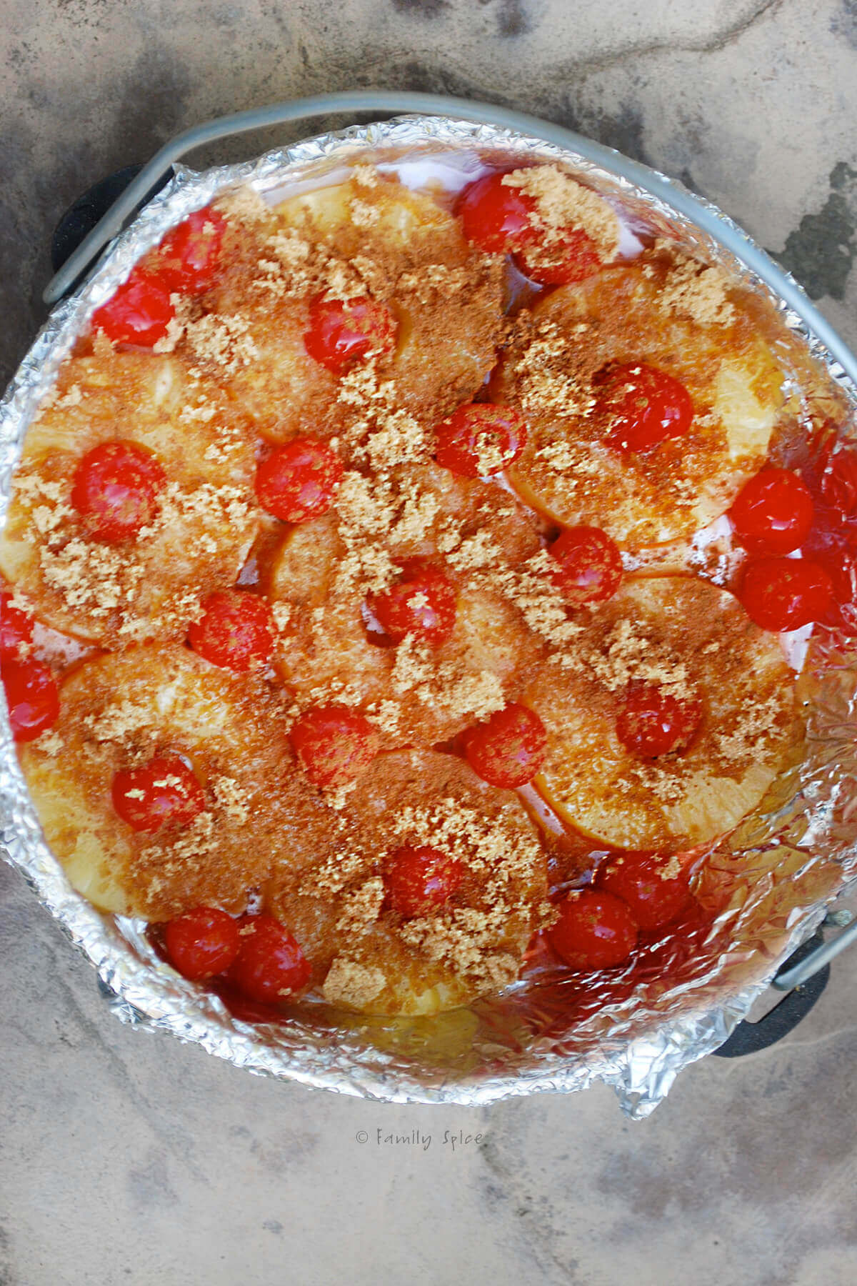 Top view of a Dutch oven lined with foil with pineapple rings, maraschino cherries and sprinkled with brown sugar