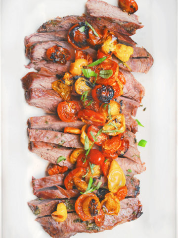 Top view of grilled flank steak cut up with roasted tomatoes on top on a white plate