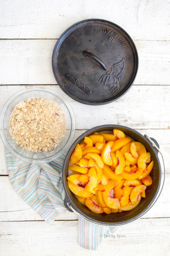 Top view of a Dutch oven with sliced peaches in it and crisp ingredients mixed in a bowl next to it