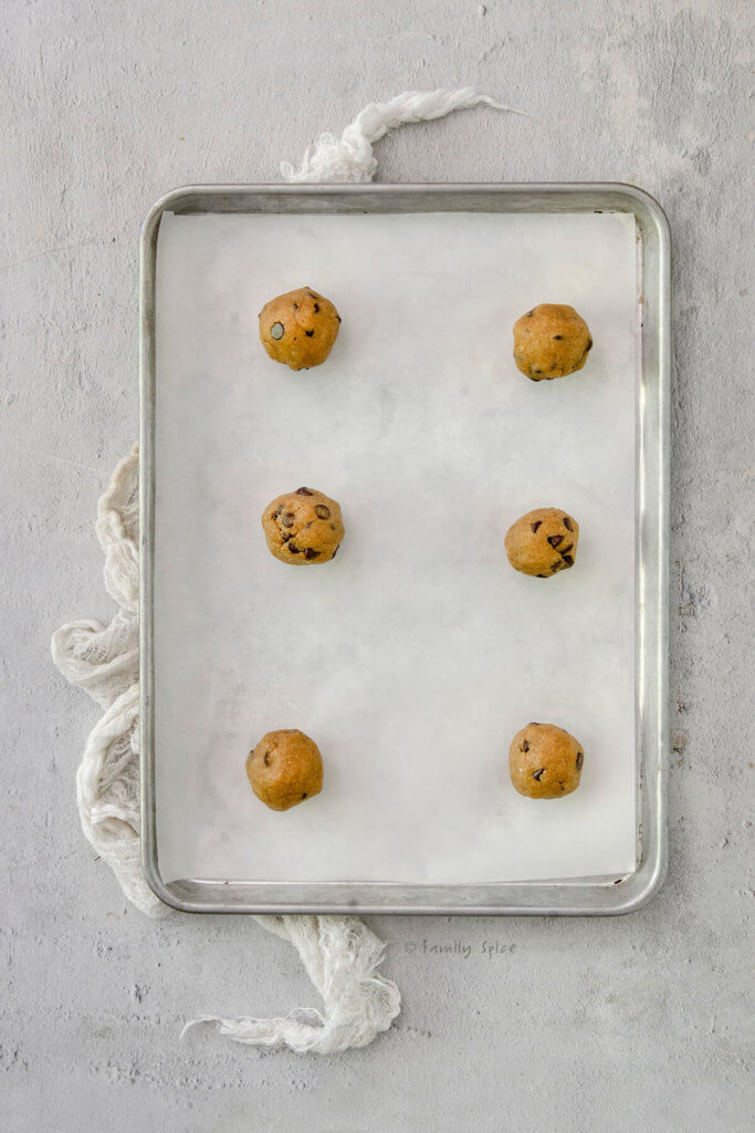 A baking sheet with six balls of chocolate chip cookie dough rolled into balls on it