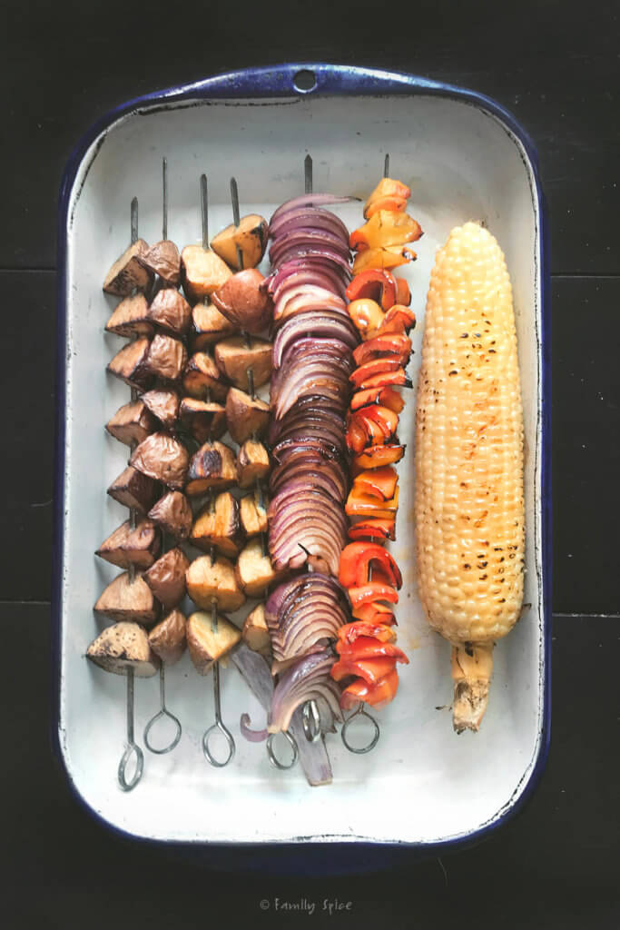 Grilled skewered potatoes, onions, bell peppers and corn on the cob in an enamel tray