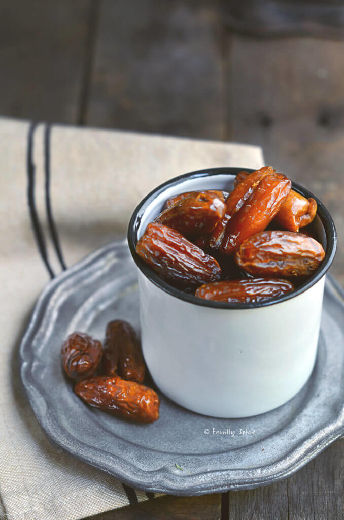 Dates sitting in a white enamel mug on a pewter plate