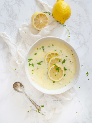 Overhead view of a bowl of chicken lemon rice soup with lemons around it